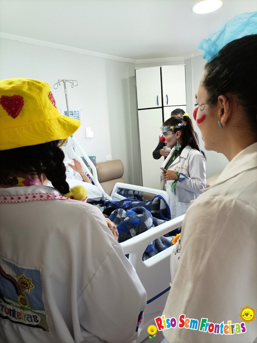 Visita humanizada no quarto de paciente — voluntárias com nariz de palhaço ao redor da cama